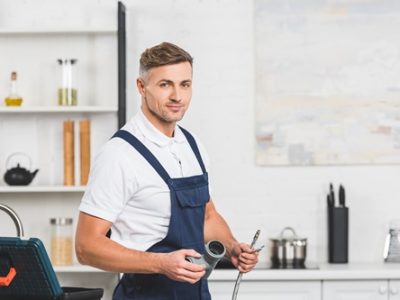 adult repairman holding pipes for kitchen faucet repairing and looking at camera